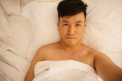 Directly above portrait of shirtless young man lying on bed