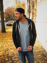 Young man standing on autumn leaves in city