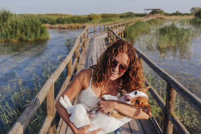 Smiling woman with dog on footbridge against sky