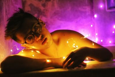 Portrait of young woman with illuminated string lights in darkroom