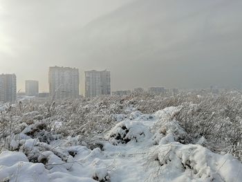 Snow covered buildings in city against sky