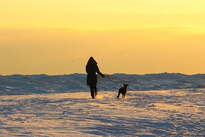 Rear view of woman walking on snow covered landscape during sunset