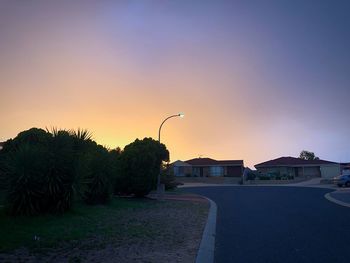 Street by buildings against sky during sunset