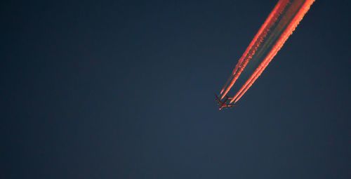 Low angle view of airplane flying with vapor trails in clear blue sky