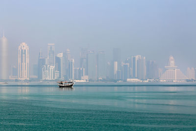 Boat in sea against modern buildings in city on a foggy day