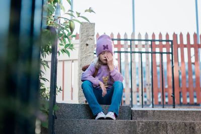 Young girl looking stressed sat on a step waiting for school