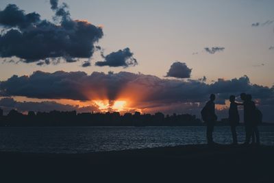 Silhouette couple standing on beach against sky during sunset