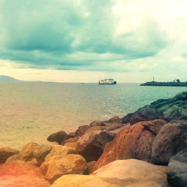 sea, water, sky, transportation, scenics, nautical vessel, beauty in nature, tranquility, tranquil scene, cloud - sky, mode of transport, horizon over water, rock - object, nature, boat, cloudy, idyllic, cloud, mountain, shore