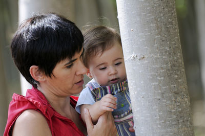 Close-up of mother and baby daughter looking at tree trunk