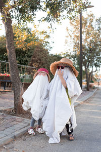 Trendy sheet ghosts costumes on little kids standing on a suburbs street. happy halloween holiday