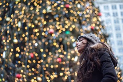 Woman looking at illuminated christmas tree in city during winter