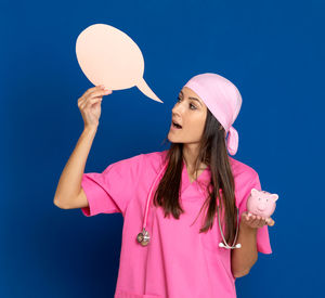 Young woman looking away while standing against blue background