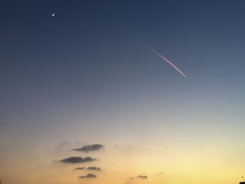 Low angle view of vapor trail and moon against sky at dusk
