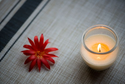 Close-up of lit tea light candle by red flower on table