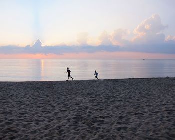 People walking on beach against sky during sunset