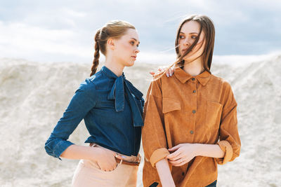 Fashion beauty portrait of young women sisters in brown velvet jeans shirts on the desert background