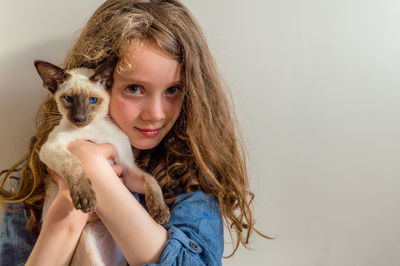 Portrait of girl holding cat against wall