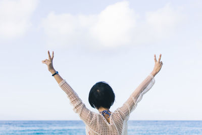 Rear view of woman standing at beach against sky