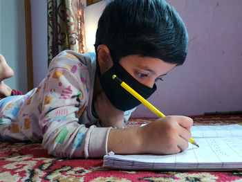 Boy wearing mask writing in book
