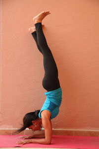 Young woman practicing handstand by wall