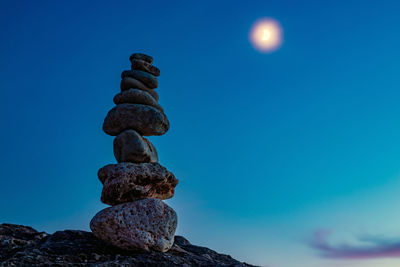 Stack of stones on rock by sea against blue sky