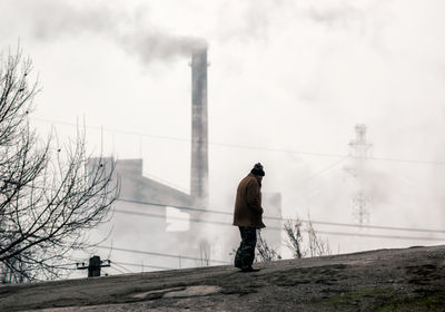 Rear view of man standing on factory against sky