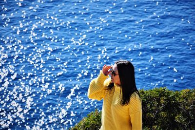 Woman photographing by sea against blue sky