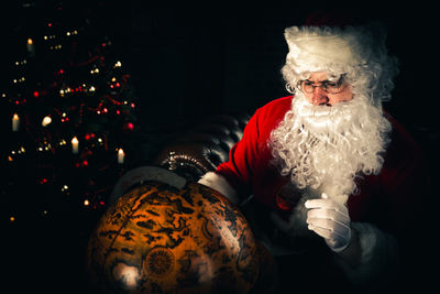 Man wearing santa claus costume looking at globe at home