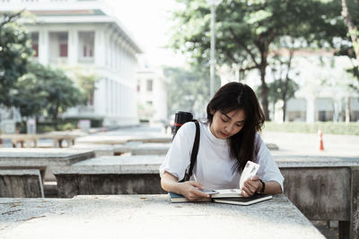 Full length of woman sitting on book against building