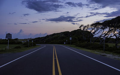 Empty road by trees against sky