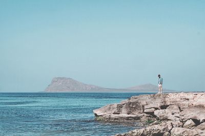 Rear view of woman standing on rock by sea against clear sky