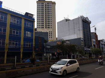 Cars on road by buildings in city against sky