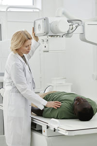 Doctor instructing patient lying on x-ray machine in clinic