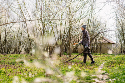 Full length of man holding axe amidst trees in spring