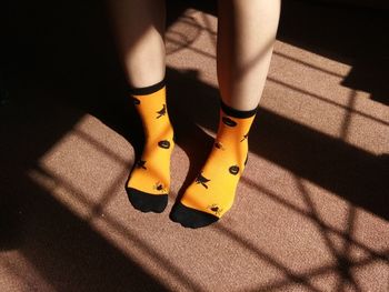 Low section of woman wearing yellow socks while standing on carpet at home