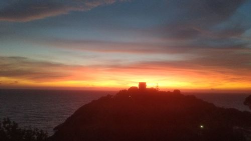 Silhouette buildings by sea against sky during sunset