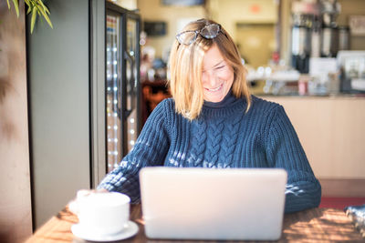 Mid adult woman using mobile phone while sitting on table