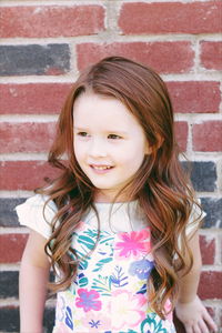 Portrait of smiling girl standing against red brick wall