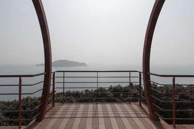 Empty footbridge in forest against sea and sky