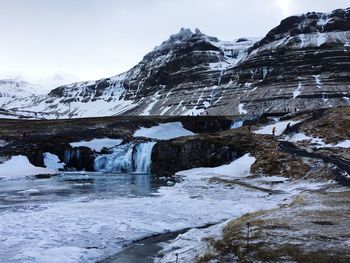 Frozen lake by snowcapped mountain against sky