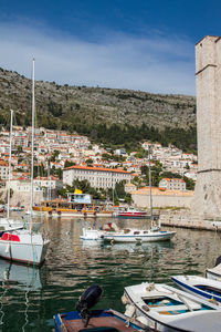 Boats moored at harbor by buildings against sky