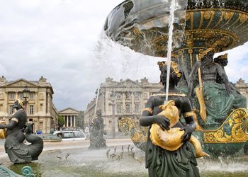 Statue by fountain in city against sky