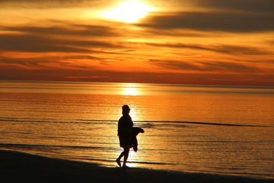 Silhouette woman on beach against sky during sunset