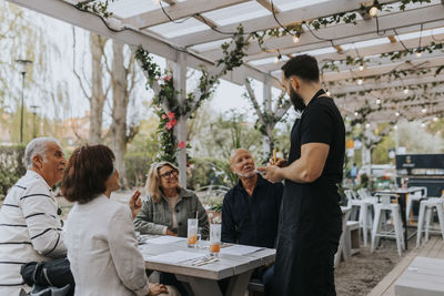 Male and female senior friends giving food order to waiter standing at restaurant