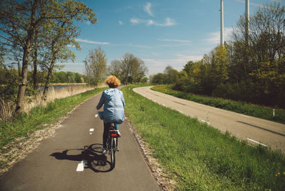 Rear view of woman with curly hair riding bicycle on road