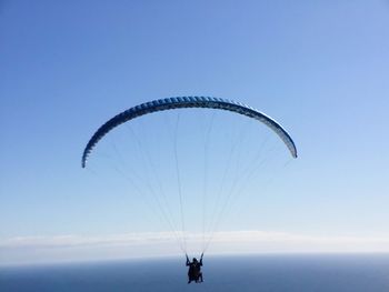 Man paragliding over sea against clear sky