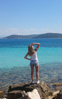 Rear view of woman standing on rock against sky