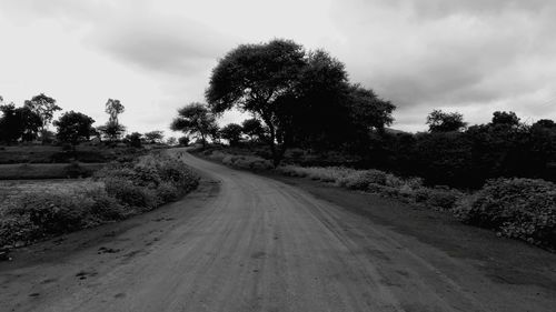 Road passing through field against cloudy sky