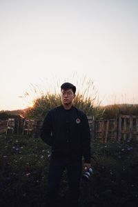 Portrait of young man standing on field against sky