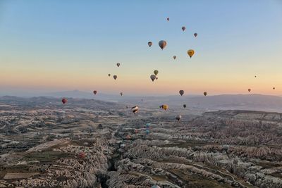 Hot air balloons flying over landscape against clear sky during sunset